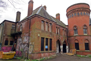 View of red brick two-storey building with round tower; graffiti and boarded up windows